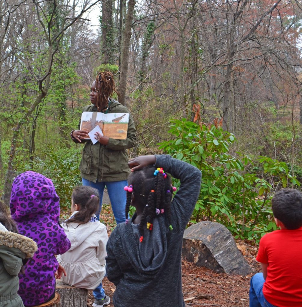 Tarneshia Evans reading a story to a field trip class at the "amphitheater" along the Tree Trail in the Children's Garden. 