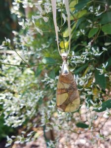 Paper Kite Butterfly wing pendant held against small white flowers