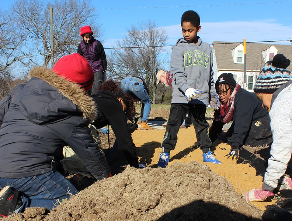 Group working together spreading sand, while kid plays king of the hill in an urban gardening project.