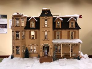 Large exterior view of a Victorian dollhouse decorated for the holidays, with cotton snow