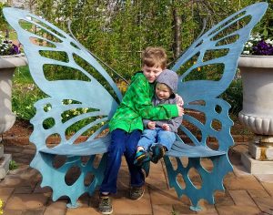 Boys hugging each other on a butterfly bench outside of the Conservatory at Butterflies LIVE! at Lewis Ginter Botanical Garden.