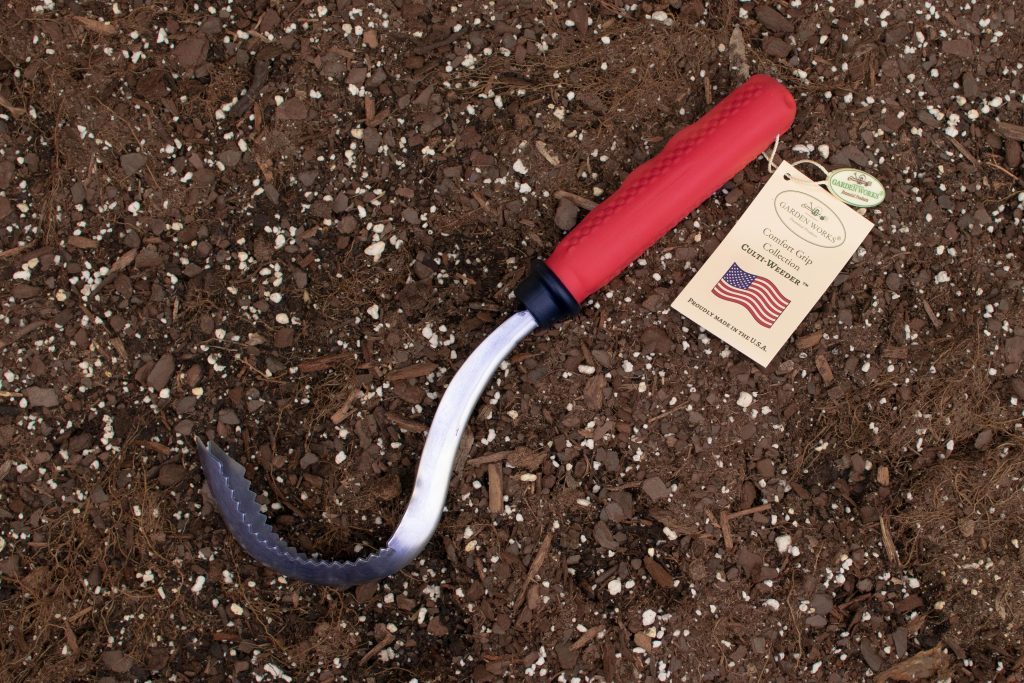 garden weeder tool with a red handle and attached price tag laying in soil 