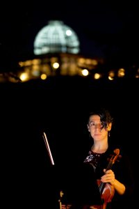 a violinist in the dark with just a small amount of light and the Conservatory in the background. Image by Harlow Chandler