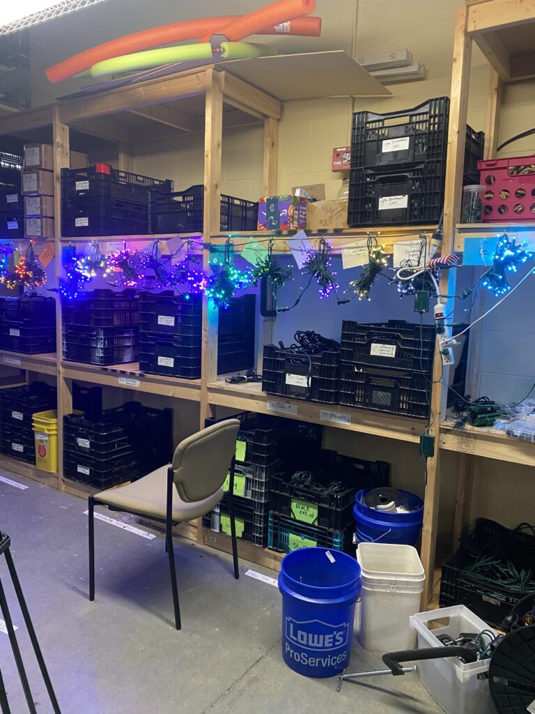 The color wheel of lights in the KEC basement. A shelving unit with crates full of string lights. Photo by Meredith Orne.